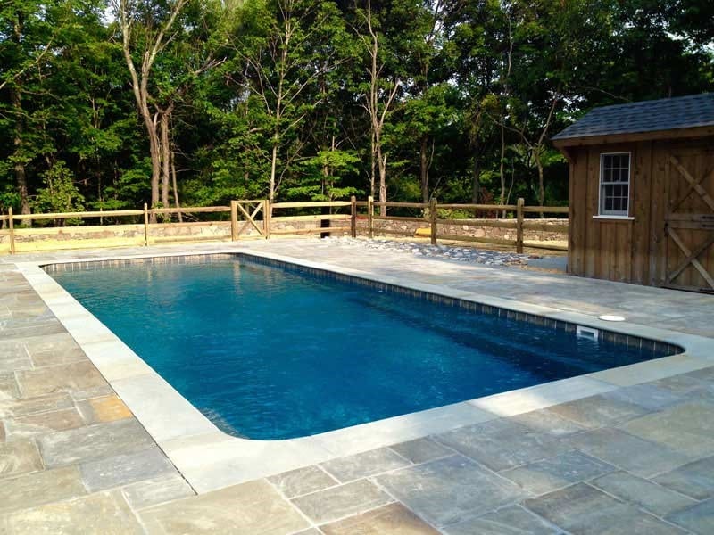 A pool with a wooden fence and trees in the background.